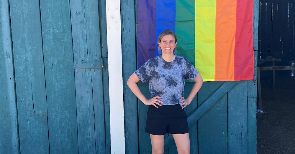 Creative Director Emily Clark standing in front of a barn with a rainbow Pride flag behind her