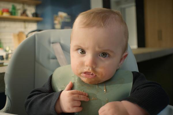 Baby wearing a green bib with baby food on face