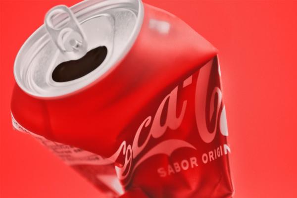 A crushed can of Coca-Cola against a red background