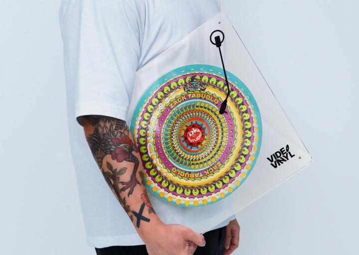 Person holding a Coke Studio limited edition Video Vinyl with one tattooed arm by their side. The vinyl features a colorful spiral pattern of blue, red and yellow