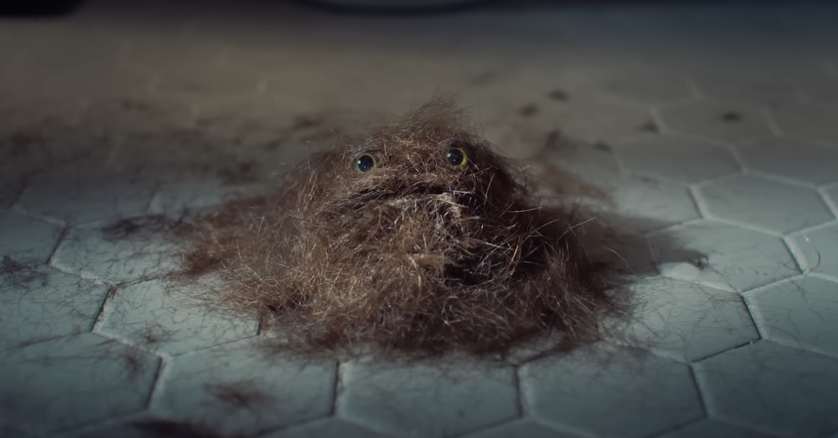 Clump of hair with eyes and a mouth on a tile bathroom floor - from Manscaped Super Bowl ad