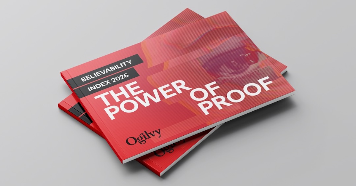 A mockup of two printed copies of the Ogilvy report, titled "Believability Index 2026: The Power of Proof," stacked slightly offset on a plain grey surface. The landscape-oriented brochure features a bold red cover with the main title "THE POWER OF PROOF" printed in a large, white sans-serif font. In the top-left corner, a dark grey rectangle contains the white text "BELIEVABILITY" above a smaller grey box reading "INDEX 2026." The black "Ogilvy" logo is positioned in the lower-left corner. The background of the cover has a textured red design featuring a subtle, close-up overlay of a human eye.
