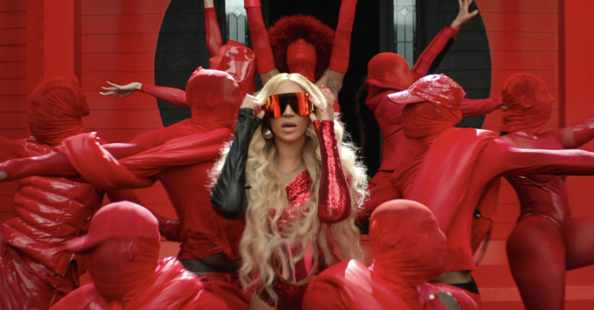 Beyonce emerging from a red house in a red dress and sunglasses flanked by dancers in water wearing red