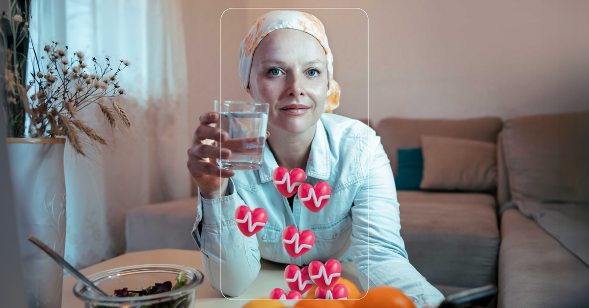 A woman sitting inside a living room looking at the camera smiling, holding a glass of water. She wears a head covering. She is framed by the thin outline of a smartphone, and there are small red heart icons with a pulse line on them emanating from the phone outline 