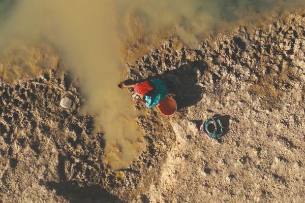 Overhead shot of a person in a sandy desert retreiving water 