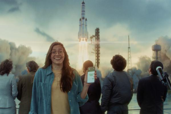 Woman holding up her phone facing the camera while a rocket launches in the background
