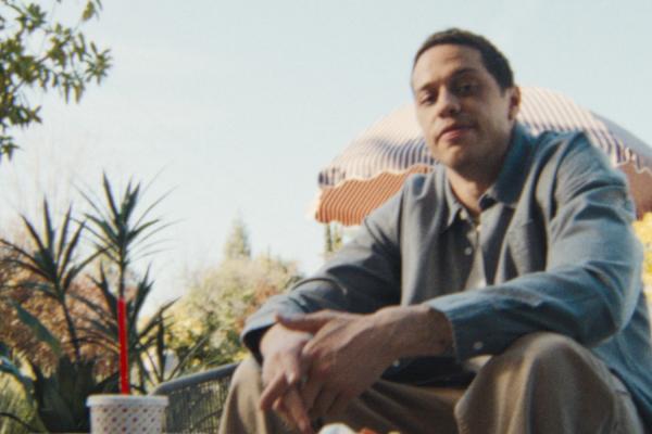Pete Davidson sitting outside with a fast food meal on a table in front of him