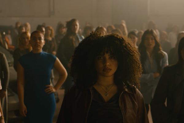 Young woman looking into the camera, in the background spread out are various other women who are all posing and looking into the camera
