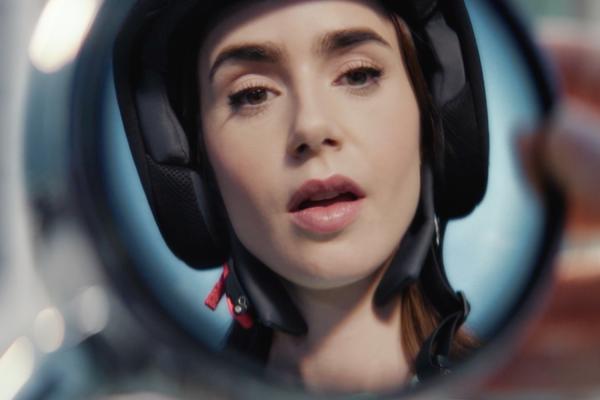 Lily Collins wearing a moped helmet, her face reflected in a rear-view mirror