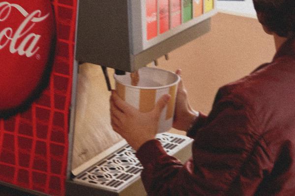 Grainy image of someone filling up a large bucket with Coca-Cola from a soda fountain