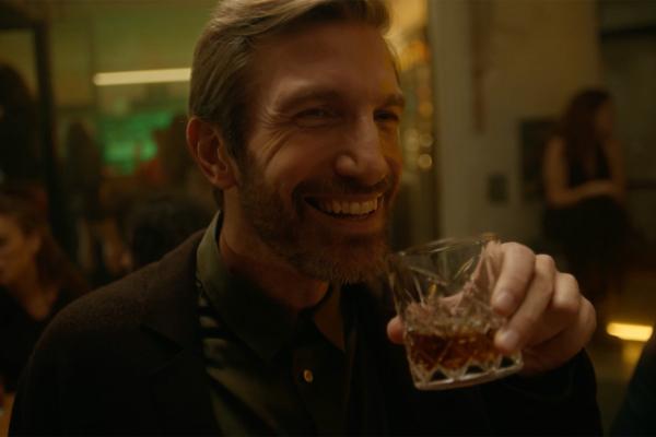 close up of bearded man smiling holding a small cocktail glass