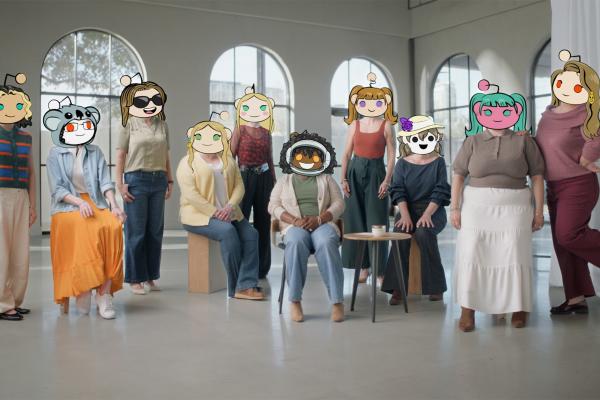 A diverse group of ten women of various ages and body types are standing and sitting in a well-lit room with arched windows. Each woman's face is covered by a unique Reddit avatar.