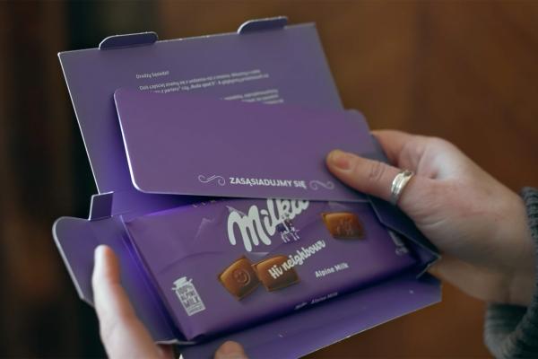 Hands opening a purple gift box containing a Milka chocolate bar.