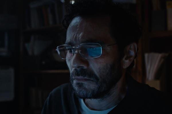 A man in glasses staring at a computer screen which is off screen