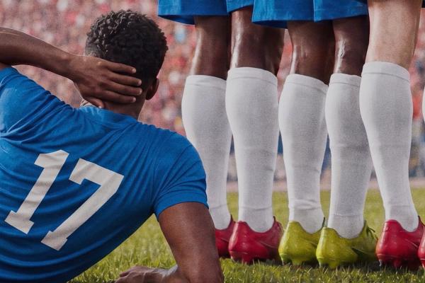 Soccer player in blue jersey with white number 17 on it lying down with hand to back of neck. he lies behind the legs of teammates with high white socks