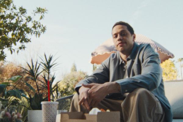 Pete Davidson sitting outside with a fast food meal on a table in front of him