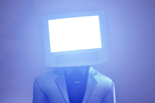 Image of a person in a suit, with a monitor in place of a head. The monitor is on and emitting a bright light