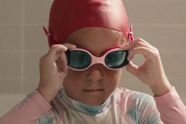 Young child in swim cap putting on swimming goggles