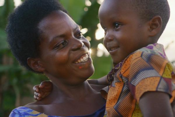 Rwandan mother holding her child outside with trees in the background, both smiling
