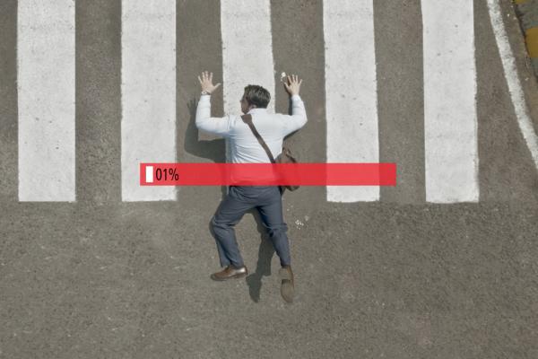 Bird's eye view of man lying on the street in the middle of a crosswalk with a video game style power bar empty in red in the middle of the frame