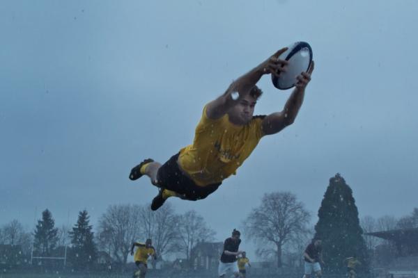 Rugby player in a yellow uniform flying through the air holding the football while outstretched