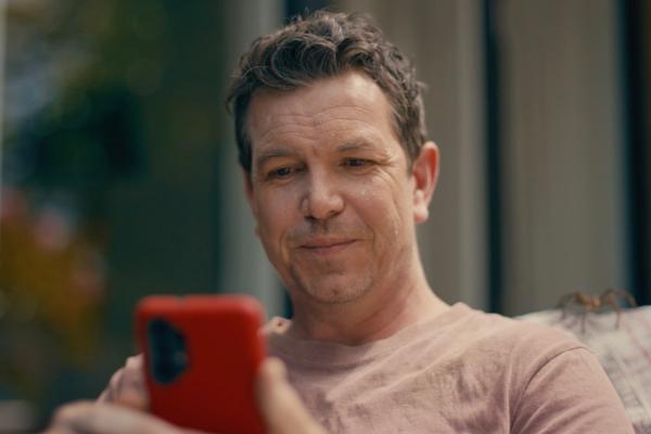 Man with short brown hair sitting outside in a t shirt looking at his phone