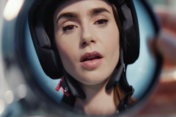 Lily Collins wearing a moped helmet, her face reflected in a rear-view mirror