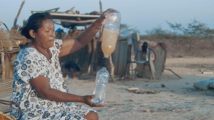 Colombian woman outside pouring water from one bottle into another bottle with a Filter Cap affixed to the top