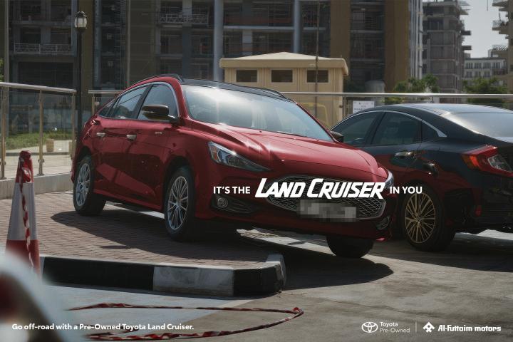 It's the Land Cruiser in you — Al-Futtaim Toyota Red car parked half on curb and half on road. White copy overlay "It's the Land Cruiser in You"