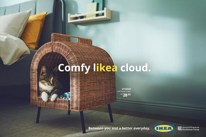 LIKEA — IKEA Cat lying in a wooden indoor cat bed with text overlay "Comfy likea cloud" with "likea" in yellow