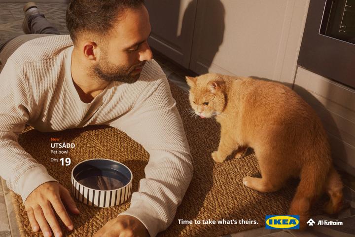 Time to Take What's Theirs — Al-Futtaim IKEA A man lying on the floor near a cat's water bowl, with the cat looking at hom