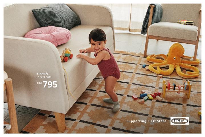Supporting First Steps — Al-Futtaim IKEA A baby stands with the help of a couch. On the floor are kids toys -- wooden blocks and a stuffed animal octopus