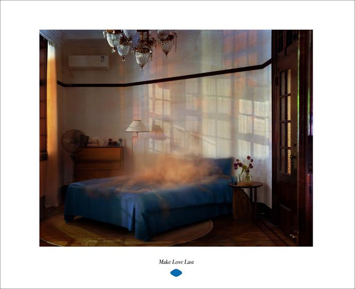 Make Love Last — Viagra A bedroom bathed in sunlight, with shadows of window panes cast across the wall behind a blue-covered bed. A vintage chandelier hangs from the ceiling, and a partially open wooden door is visible on the right. The text 'Make Love Last' appears below the image.
