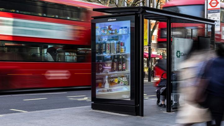 Hiders Keepers — Stella Artois Image of an outdoor advertisement on the side of a bus stop. There are fast moving objects in the background and foreground -- a red bus, people walking. The advertisement shows an open refrigerator crowded with many items.