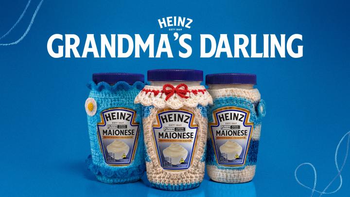 hree jars of Heinz Mayonnaise are shown on a blue background, each covered in a unique, handmade crocheted cozy. The left jar has a blue cozy with a yellow flower detail, the middle jar has a cream and red cozy with a small red bow, and the right jar has a blue, white, and cream striped cozy.