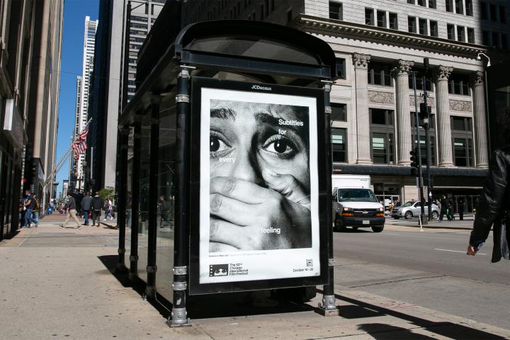 Outdoor street installation showing a Chicago International Film Festival poster in a glass transit shelter, featuring a dramatic close-up of wide eyes and a hand covering a mouth with the tagline 'Subtitles for every feeling'.