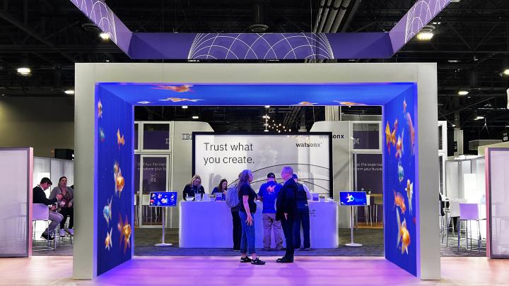 Square booth display with fish projection in front of a banner that says "Trust What You Create" and people interacting indoors at the Adobe Summit