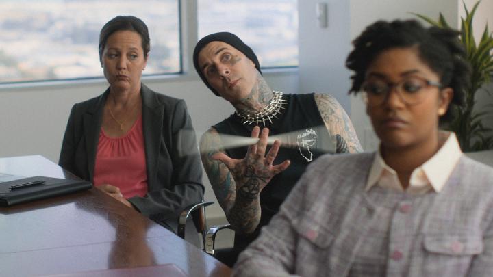 Travis Barker sitting in an office between two female office employees