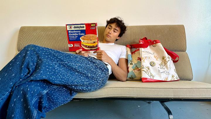 Griddle Bag — Jimmy Dean Person sitting on couch with blue blanket holding a box of Jimmy Dean, next to them on couch is Jimmy Dean Griddle Bag