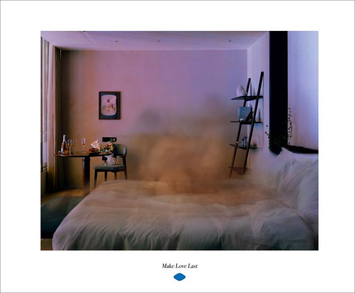 Make Love Last — Viagra A bedroom scene with a large bed covered in white linens. A table is set with champagne and flowers, and a ladder shelf stands against the wall. An ethereal, cloud-like effect obscures the center of the room. The text 'Make Love Last' is displayed below.