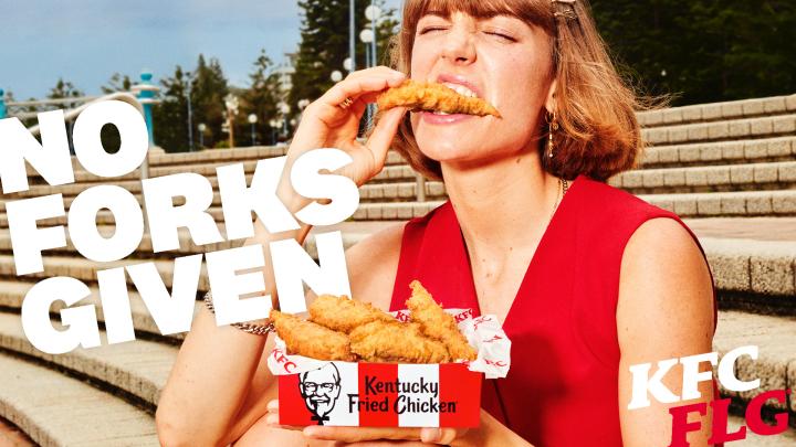 KFC FLG — KFC Happy young woman holding a bucket of KFC chicken and about to eat a piece. White copy superimposed over image: No forks gievn