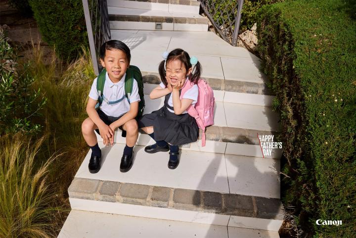Behind the Scenes Dads — Canon Two happy kids sitting on their front steps with backpacks on