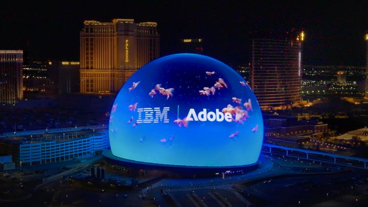IBM and Adboce logos projected on the Sphere in Las Vegas, featuring AI generated images of orange fish against a blue backdrop