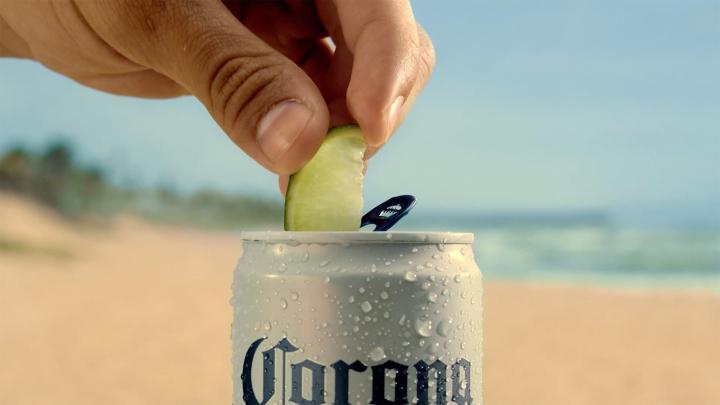 "A hand pressing a lime wedge into an ice-cold Corona can on a sunny beach."