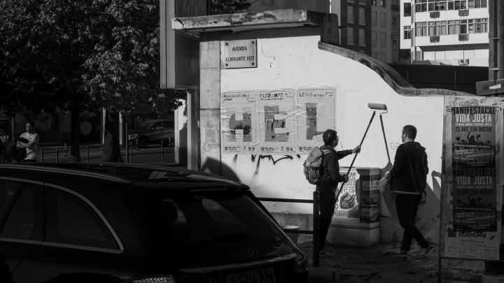 Black and White image of people pasting posters featuring the Endangered Font spelling out H-E-L