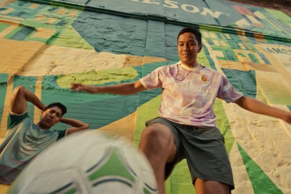 Two people playing soccer in front of a large colorful mural, with a ball in the foreground.