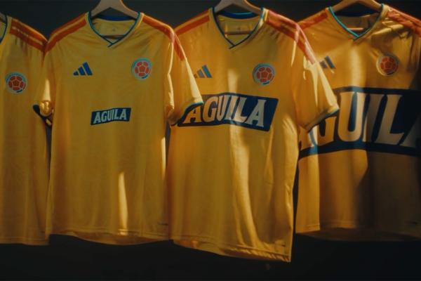 A row of yellow Colombia national football team jerseys by Adidas, each featuring the Aguila sponsor logo, hanging in a dimly lit room."