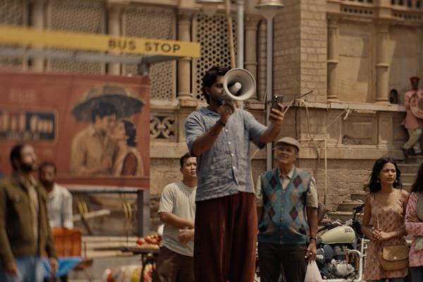 Still from PhonePe’s 10th anniversary campaign showing fast-talking talent Shahu Supreme addressing a crowd through a megaphone on a bustling Indian street.