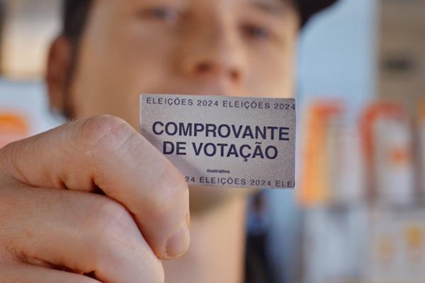 Close up of a person holding a small receipt in front of their face. It says "Comprovante de Votação"