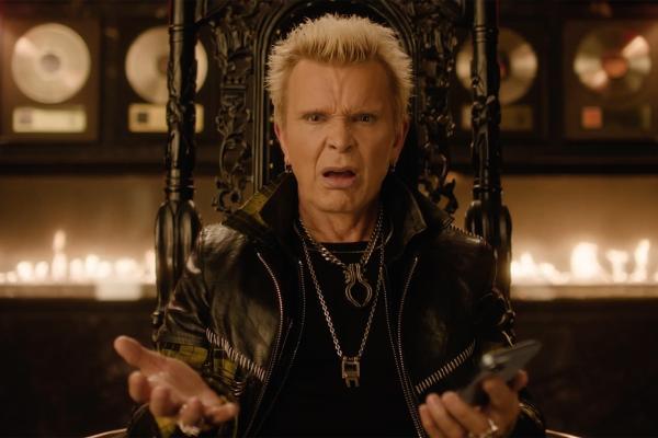 Billy Idol sitting on a throne with a line of flames in the background